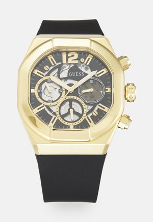 Goldfarbene Edelstahl-Armbanduhr mit achteckigem Gehäuse, schwarzem Zifferblatt, weißen und goldenen Akzenten, schwarzem Gummiband und drei Zifferblättern für Chronographenfunktionen.