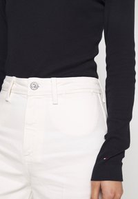 Musta ribbineuloksinen pitkähihainen paita yhdistetty valkoisiin farkkuihin, joissa on nappikiinnitys, vyölenkit ja hillitty ompelu.