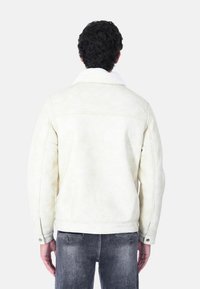 Giacca bianca foderata in shearling sintetico con colletto abbottonato, caratterizzata da una texture morbida e un design pesante, abbinata a jeans in denim grigi.