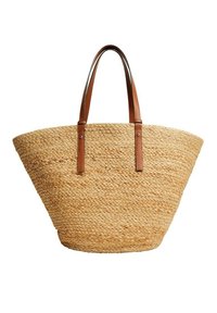 Woven straw tote bag o szerokim, trapezoidalnym kształcie z dwiema brązowymi skórzanymi uchwytami przymocowanymi metalowymi nitami.