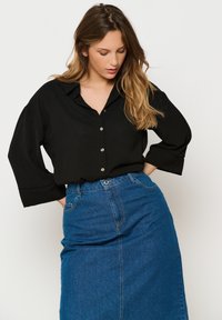 Black button-up blouse with a collar and three-quarter sleeves, paired with a blue denim skirt. Smooth fabric with a relaxed fit.