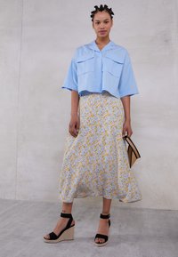 Sky blue cropped shirt with two front pockets, paired with a floral midi skirt featuring yellow and gray blooms, worn with black wedge sandals.