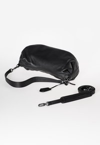 Schwarze Ledertasche mit runder Form, strukturiertem Finish, verstellbarem Riemen und Reißverschlussverschluss. Enthält einen abnehmbaren Riemen.