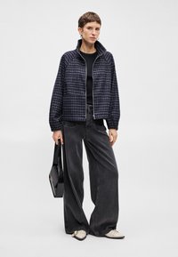 Θαλασσί check φούτερ με τσέπες και όρθιο γιακά, συνδυασμένο με φαρδιά σκοτεινά γκρι τζιν και μαύρη τσάντα, που τονίζεται από off-white παπούτσια.