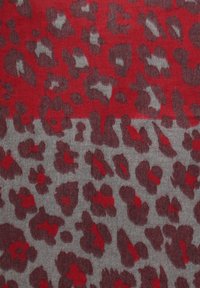 Strukturierter Stoff mit einem auffälligen Leopardenmuster in Rot und Grau, das unregelmäßige Flecken in Schattierungen von Rot und Dunkelgrau zeigt.