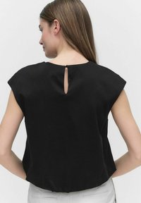 Czarna bluzka z krótkimi rękawami, z otworem w kształcie łezki na plecach i luźnym krojem. Wykonana z gładkiego materiału bez widocznych wzorów.