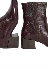Burgundy leather ankle boots with a block heel. Features a side zipper and a smooth, shiny texture. Sleek design with a tapered toe.