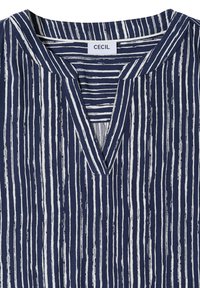 Chemise bleu marine à col avec des rayures verticales blanches irrégulières et un col en V, portant une étiquette de marque "CECIL" à l'intérieur du col.