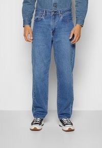 Jean en denim bleu clair avec une coupe décontractée, comprenant des poches avant traditionnelles, une fermeture à bouton et des détails de surpiqûres contrastées.