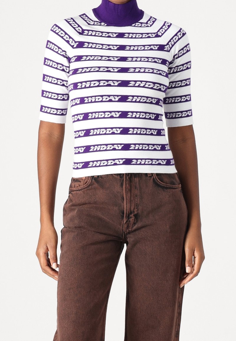 Col roulé à manches courtes rayé violet et blanc avec le texte « 2NDDAY », associé à un pantalon marron taille haute.
