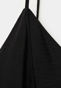 Gros plan sur un tissu noir avec une couture centrale et une fine lanière suspendue sur un fond blanc.