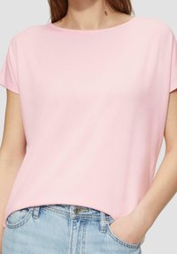 Różowa bluzka z krótkim rękawem o okrągłym dekolcie, wykonana z gładkiego materiału, noszona z jasnoniebieskimi dżinsami, w luźnym fasonie, minimalistyczny design.