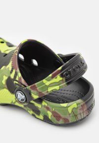 Černé a zelené maskáčové Crocs s texturovanou podrážkou, nastavitelným popruhem a logem. Vyrobené z lehkého a odolného pěnového materiálu.