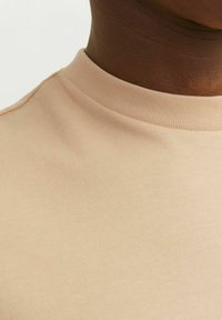 Beige bomulds T-shirt med rund, ribbet halsudskæring, med glat tekstur og uden synlige mønstre eller accenter, beskåret visning af stoffet.