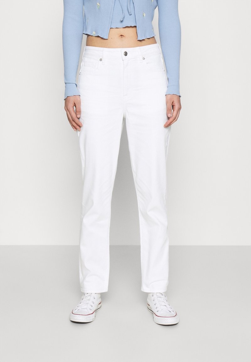 Vita denimjeans med rak passform, försedda med framfickor och kombinerade med vita sneakers. Utseendet fulländas med en ljusblå kort topp.