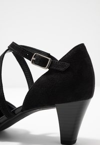 Zwarte suède hoge hak schoenen met een spitse neus, met gekruiste banden en een zilveren gesp detail op de enkelband.