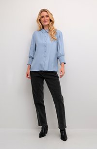 Himmelblaues Hemd mit langen Puffärmeln und gerafften Manschetten. Kombiniert mit schwarzen, geraden Jeans und schwarzen, hohen Ankle-Boots.