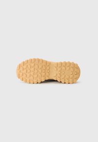 Czarne sneakersy z teksturowaną gumową podeszwą, posiadającą wzór plastra miodu. Jasnobrązowy kolor podeszwy kontrastuje z cholewką.