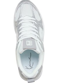 White athletic shoe featuring a mesh upper with silver accents, flat laces, padded collar, and light blue insole with a signature design.