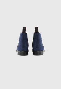 Botas de tobillo de ante azul marino con suela de goma negra, acabado texturizado y tiradores en rojo en la parte posterior para ponerlas y quitarlas fácilmente.