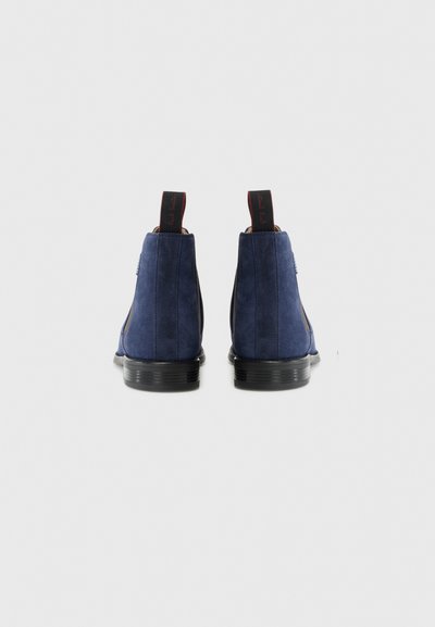 Bottines en suede bleu marine avec une semelle en caoutchouc noir, une finition texturée et des poignées de tirage rouges à l'arrière pour un enfilage facile.