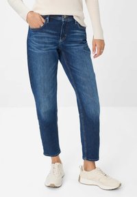 Jeans in denim blu con una vestibilità rilassata, dotati di tasche laterali, una leggera sfumatura e cuciture a contrasto, abbinati a sneaker chiare.