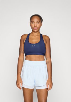 Sujeción deportiva azul marino con logo blanco, combinada con pantalones cortos de un azul claro. La tela es suave, y los pantalones cortos tienen una cinturilla elástica y ribete.