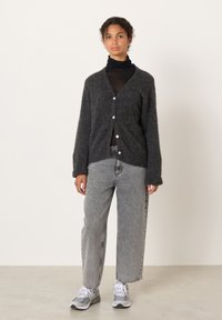 Charcoal gray wool cardigan with V-neck, front buttons, and ribbed cuffs, layered over a black turtleneck and paired with loose gray jeans.