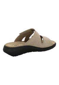 Beige open-toe slide sandal with adjustable strap, cushioned footbed, and black textured sole, angled to show side and back view.