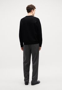 Maglione nero lavorato a maglia con collo rotondo, abbinato a pantaloni grigi a fantasia. L'outfit ha una vestibilità comoda, con dettagli a coste su polsini e orlo.
