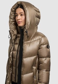 Dunjakke i dæmpet guld med høj krave og stor hætte. Fremstillet af skinnende, quiltet materiale med lynlåslukning og logodetalje.