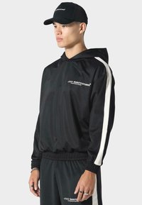 Giacca nera con cappuccio realizzata in tessuto liscio con strisce bianche laterali; presenta un elastico in vita e ai polsi, logo sul petto.