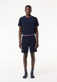 T-shirt in cotone blu navy con collo rotondo e taschino, abbinato a pantaloni corti coordinati con vita elastica. Calzini a righe completano l'outfit.