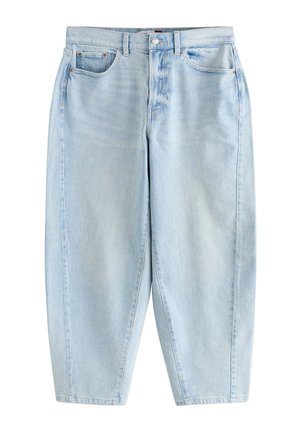Kvinde med langt mørkt hår iført en blå ternet kortærmet skjorte med knapper, lyst vaskede jeans og hvide åndbare slip-on sko.