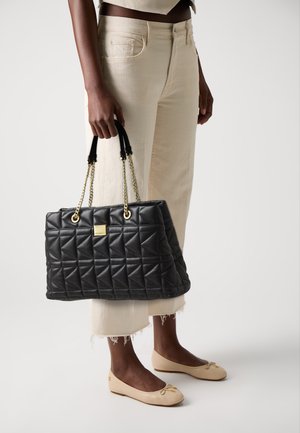 Black quilted handbag with triangular pattern, gold hardware, and dual handles. Paired with light-colored pants and beige ballet flats.
