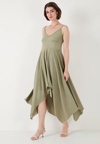 Olive green, knee-length dress with a v-neck, spaghetti straps, and an asymmetric hemline. Made of lightweight fabric with a textured finish.