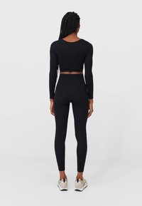 Zwarte geribbelde crop top en high-waisted leggings, fitted design. Model draagt neutraal gekleurde sneakers. Eenvoudige achtergrond.