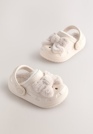 Bele klompe z mehko pentljo, teksturiranimi podplati in prezračevalnimi luknjami, s mehko notranjo oblogo in nastavljivim zadnjim trakom.