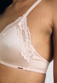 Brassière en satin rose doux avec des bordures en dentelle intricate sur les bords des bonnets et des bretelles réglables. Étiquette de la marque visible sur le côté.