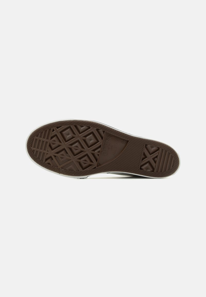 Suela de zapato de goma marrón con un patrón de agarre texturizado que presenta triángulos y líneas, rodeada de un borde blanco.