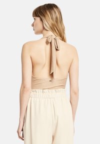 Vista posteriore di un top a halter in tessuto beige con chiusura a legaccio al collo e schiena scoperta, abbinato a giornate beige leggere e morbide.