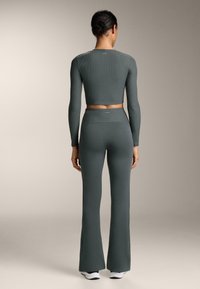 Rebrasti, dug rukav, kratki top i široke tajice u prigušenoj zelenoj boji, s visokim pojasom i suptilnim brendiranjem na leđima.