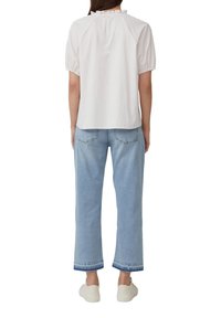 Biała i jasnoróżowa koszula w paski z falbanistym dekoltem i krótkimi bufkami, zestawiona z jasnoniebieskimi spodniami typu wide-leg i białymi trampkami.