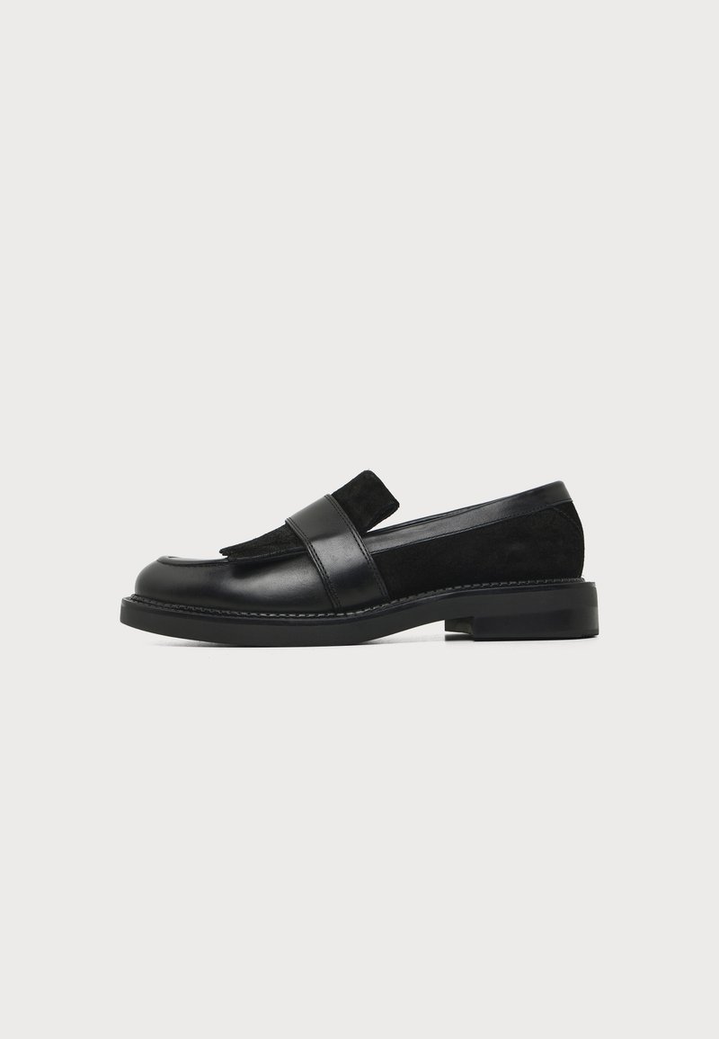 Mocassin en cuir et daim noir avec talon bas carré et une bride sur le dessus, vu de profil sur fond blanc.
