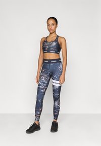 Sport bra and leggings set in blue with abstract patterns. Bra has thin straps; waistband features "STRONGER" branding. Fitted design, stretchy fabric.