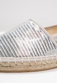 Espadrille couverte de sequins argentés avec garniture en tissu beige, semelle en jute tressée et semelle extérieure en caoutchouc, vue rapprochée de côté.