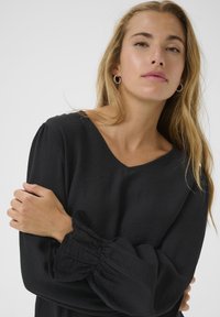 Black blouse with a V-neck, long puff sleeves, and gathered cuffs. Made of textured, soft fabric, featuring a relaxed fit.