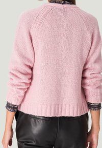 Rosa stickad tröja med raglanärmar, ribbade mudd och nederkant. Har en chunky struktur och en något kortad design. Bakåtriktad vy visas.