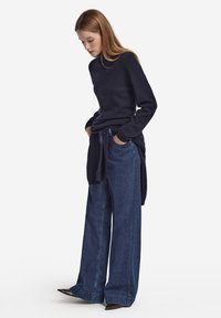 Marinblå stickad tröja med hög krage, kombinerad med lösa, vida mörkblå jeans i denim med knytband i midjan och fickor.