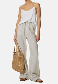 Witte cami-top, gestreepte wijde broek in beige en crème, geweven bruine schoudertas en bruine sandalen. Casual, ademende materialen.